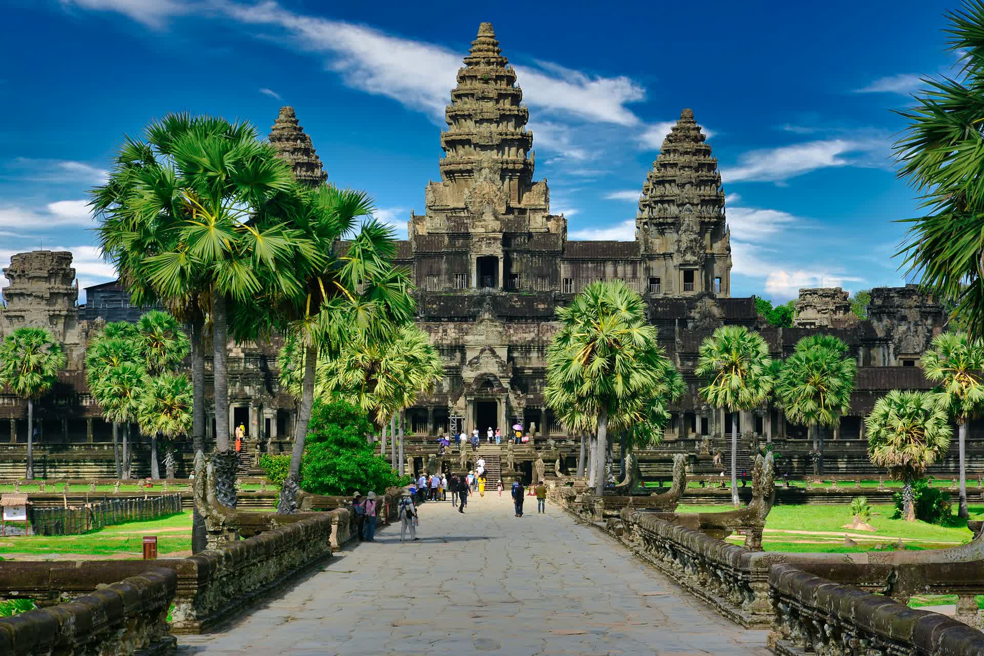 The stone towers of Angkor Wat rising above palm trees at the end of its causeway in Siem Reap