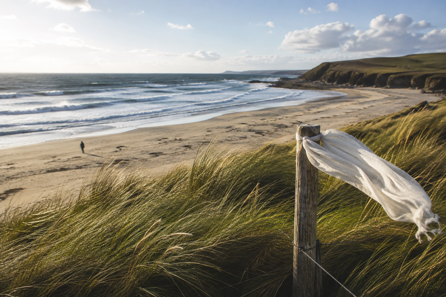Wind-shaped coastal dunes, foamy waves, a distant walker, and a linen scarf