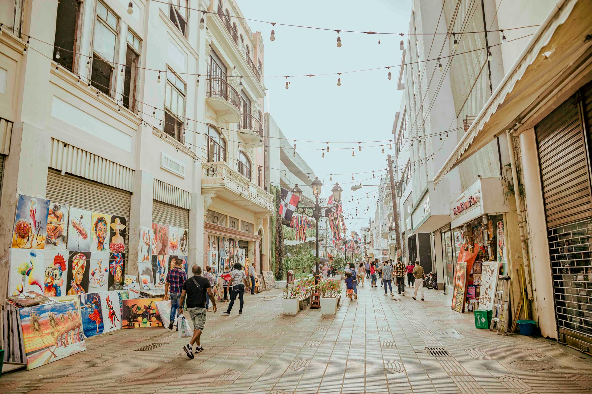 Pedestrians and street-side art stalls beneath strings of lights on Calle El Conde in Santo Domingo's Ciudad Colonial