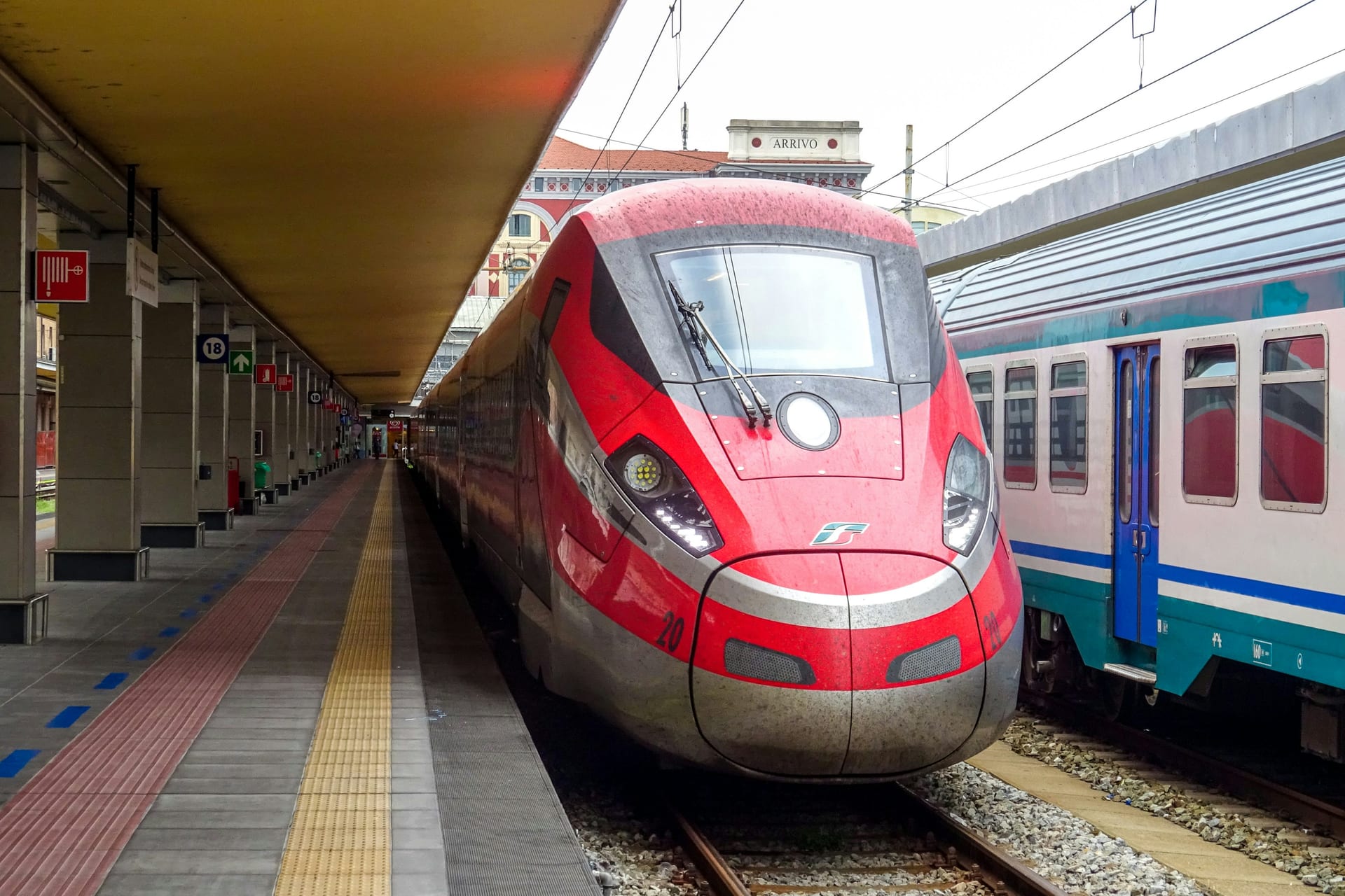 A Frecciarossa high-speed train at an Italian station platform beside a regional train
