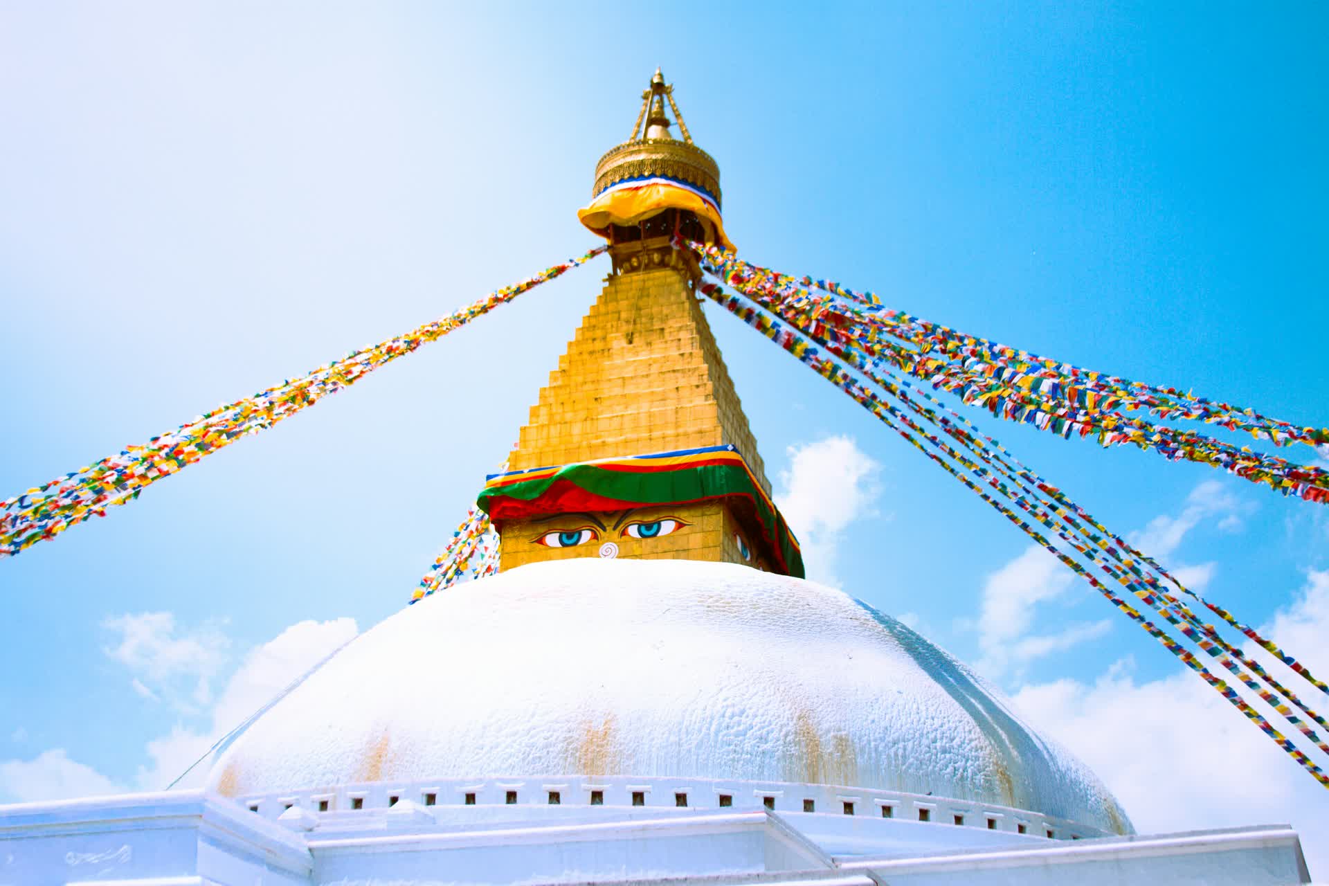 The gilded spire and painted eyes of Boudhanath Stupa in Kathmandu, strung with colorful prayer flags