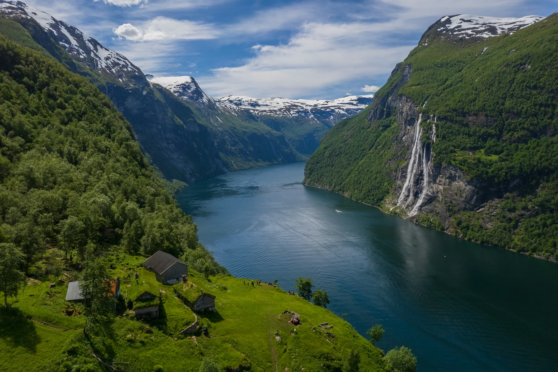 Aerial view of Geirangerfjord in Norway, with a waterfall cascading down steep cliffs into the fjord