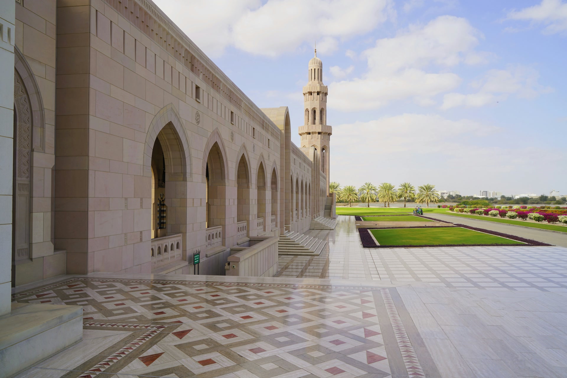 Arched colonnade and minaret of the Sultan Qaboos Grand Mosque above a marble courtyard and gardens in Muscat