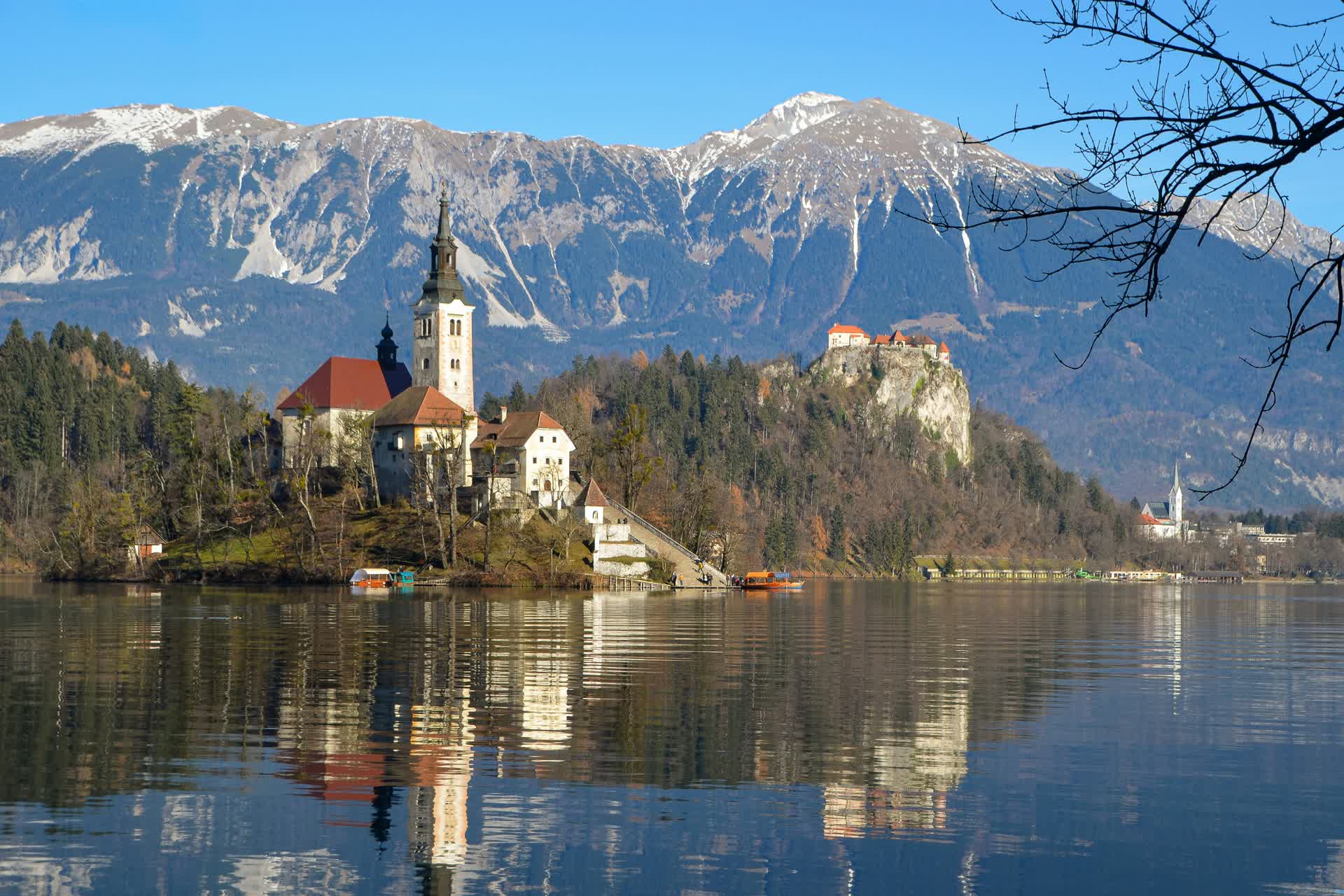 Bled Island's church and Bled Castle on a cliff above Lake Bled, with the snow-capped Julian Alps behind